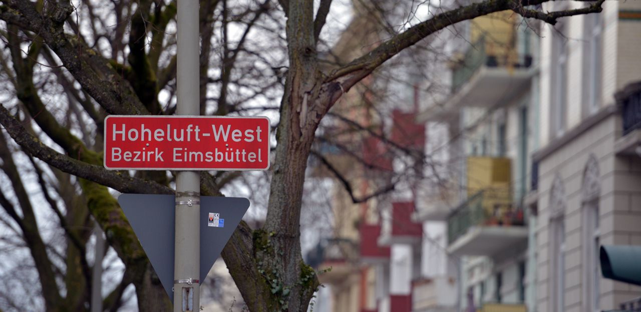Schild zum Stadtteil Hoheluft-West  mit unscharfen Gebäuden im Hintergrund